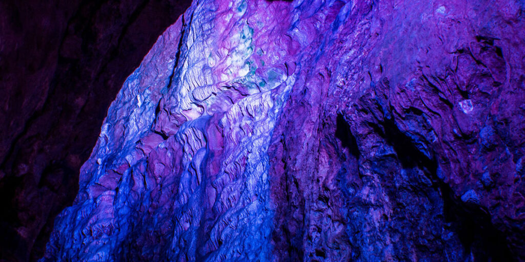 A cave wall lit up with dark blue and purple lights.